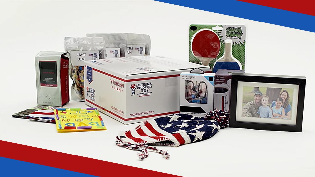  A 优先邮件 box surrounded by items that can be shipped inside it including a family photo, a hat designed to look like an american flag, 游戏桨, 生日贺卡, 干果, 咖啡, 小型电子产品.